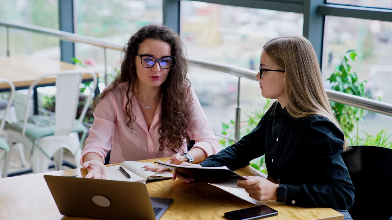 Women in office talking over business issues. Happy smiling ladies sit at the table with laptop and documentation.