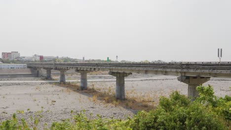 A-long-road-bridge-passing-across-a-large-dry-river-under-an-overcast-summer-sky-in-southern-Taiwan---wide-shot