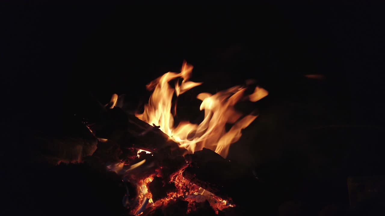 4k video enfoque selectivo primer plano de las llamas quemando leña. fogata al aire libre fogata en fondo negro por la noche.