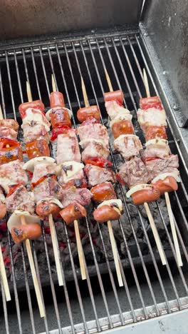 vertical video panning left to right of meat skewers on a charcoal grill, with red peppers, white onions, and sausages. glowing red coals and light smoke create a rustic, savory scene.