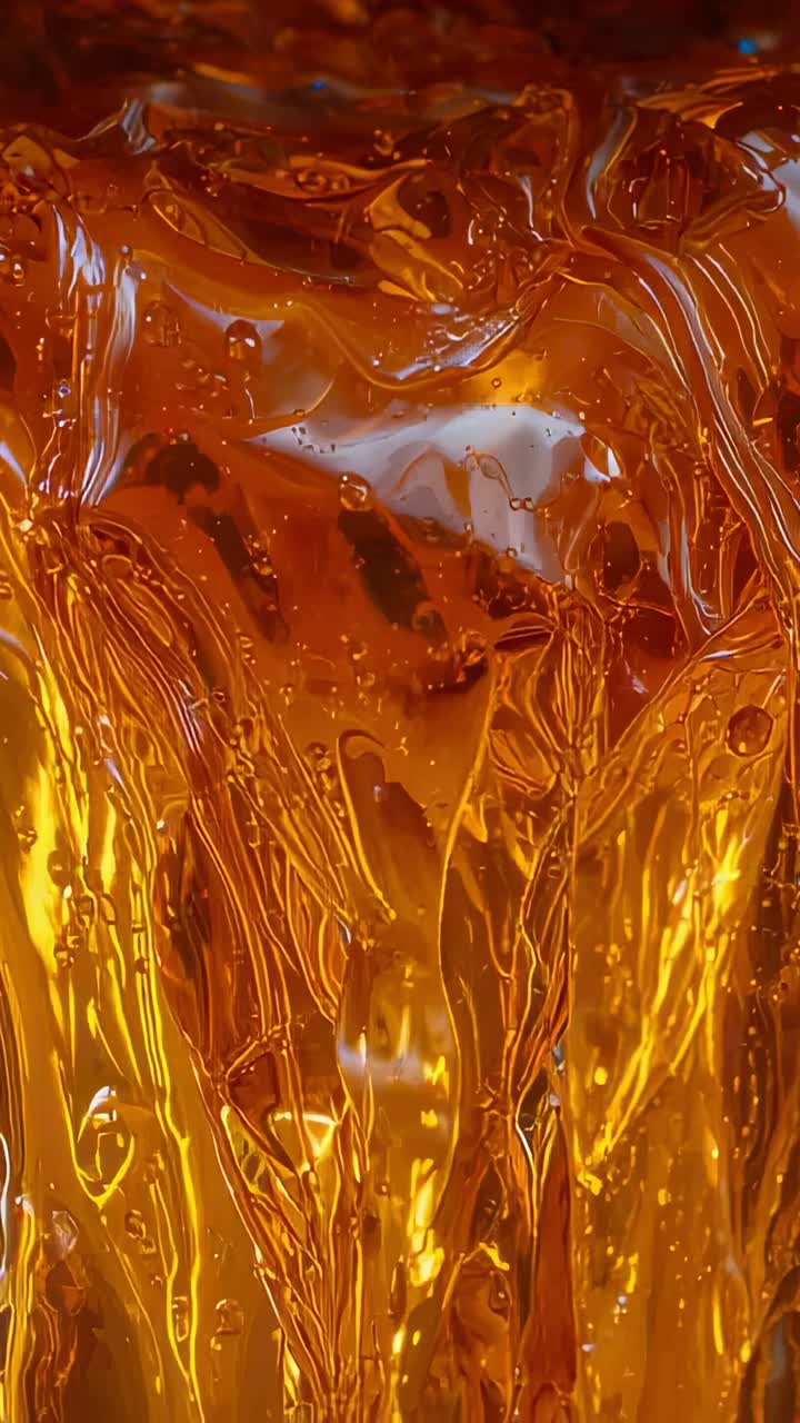 Vertical video: Camera capturing flowing amber liquid shifting texture in macro shot with foam