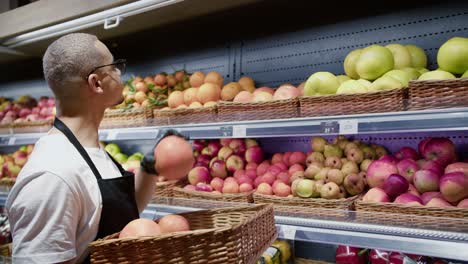 trabajador de delantal negro organizando cítricos frescos en la sección del supermercado