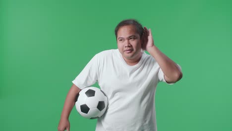 초록색 스크린 배경에서 축구를 응원하는 동안 듣기 위해 공을 는 귀를 가진 아시아 남자