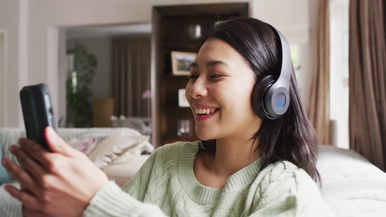 Video di una donna birazziale sorridente con capelli scuri che usa cuffie e smartphone.