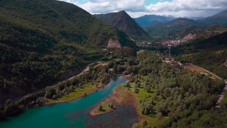 Horizontale-4K-Luftaufnahmen-Eines-Sees-In-Einer-Grünen-Natürlichen-Umgebung-Mit-Bergen-Und-Einem-Dorf