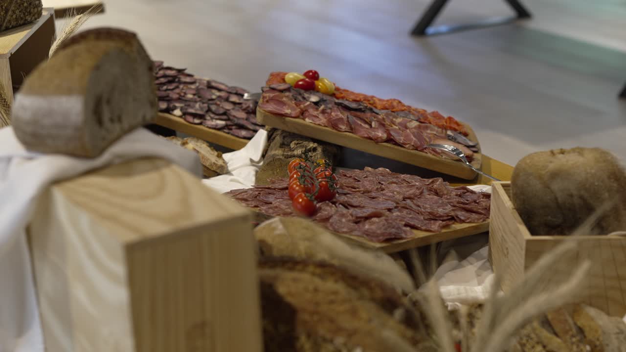 Platter of sliced meats with cherry tomatoes, accompanied by fresh bread on wooden crates