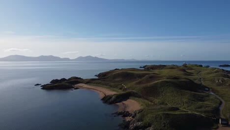 Aerial-view-across-idyllic-Ynys-Llanddwyn-island-coastline-with-hazy-Snowdonia-mountain-range-across-shimmering-Irish-sea-at-sunrise