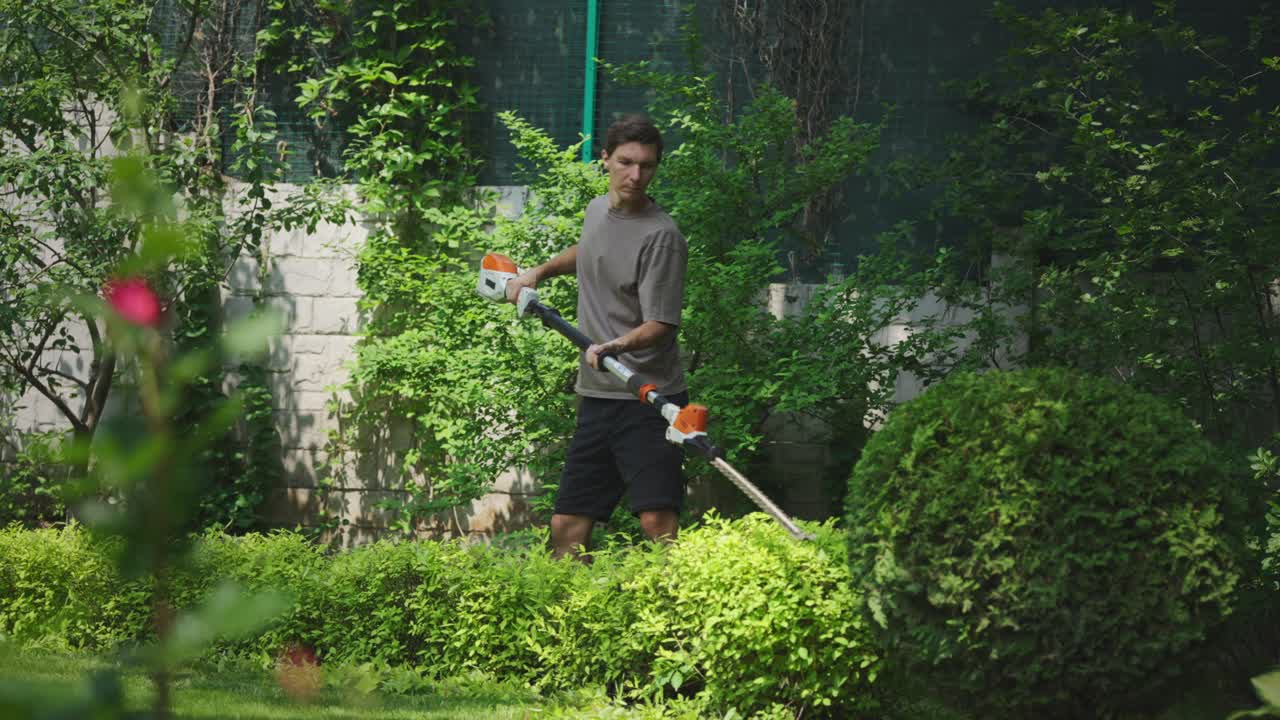 Man Trimming Hedges in a Green Garden with an Electric Trimmer