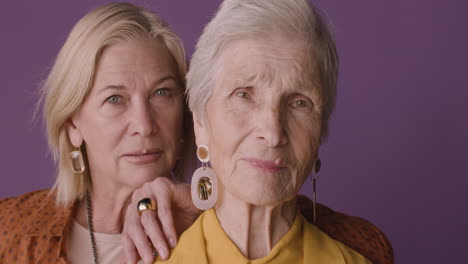 close up view of blonde mature woman with brown shirt posing with senior woman with short hair on purple background