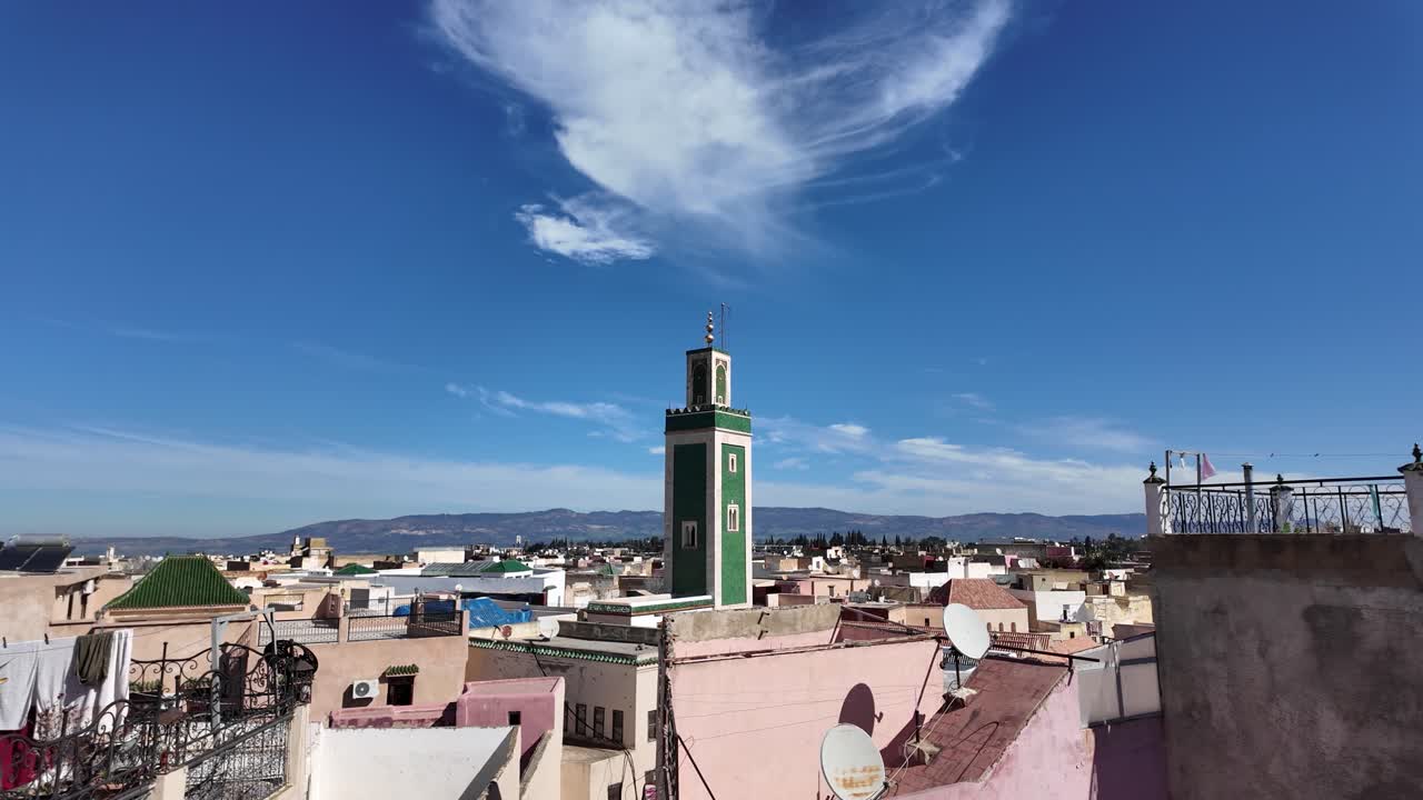 Traditional moroccan window framing the minaret of the Grand Mosque of Meknes, with a colorful lantern, under a blue sky