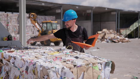 man in hardhat inspects paper bale at outdoor recycling plant, slomo