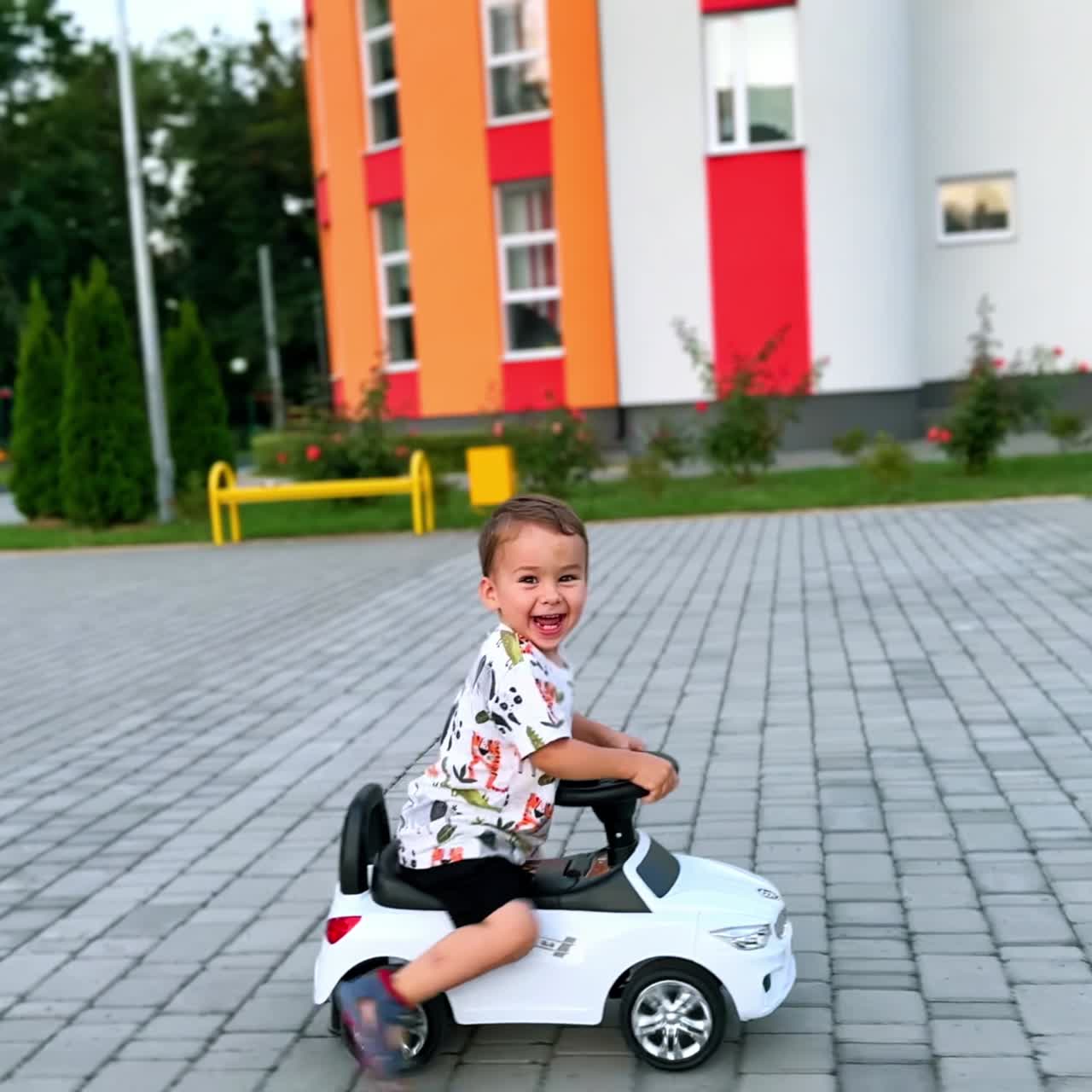 Bambino felice che guida la sua macchinina su una strada asfaltata. Bambino attivo che si muove velocemente spingendosi da terra