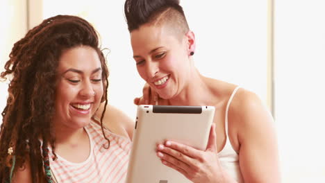 una pareja de lesbianas sonrientes usando una tableta en la cama.