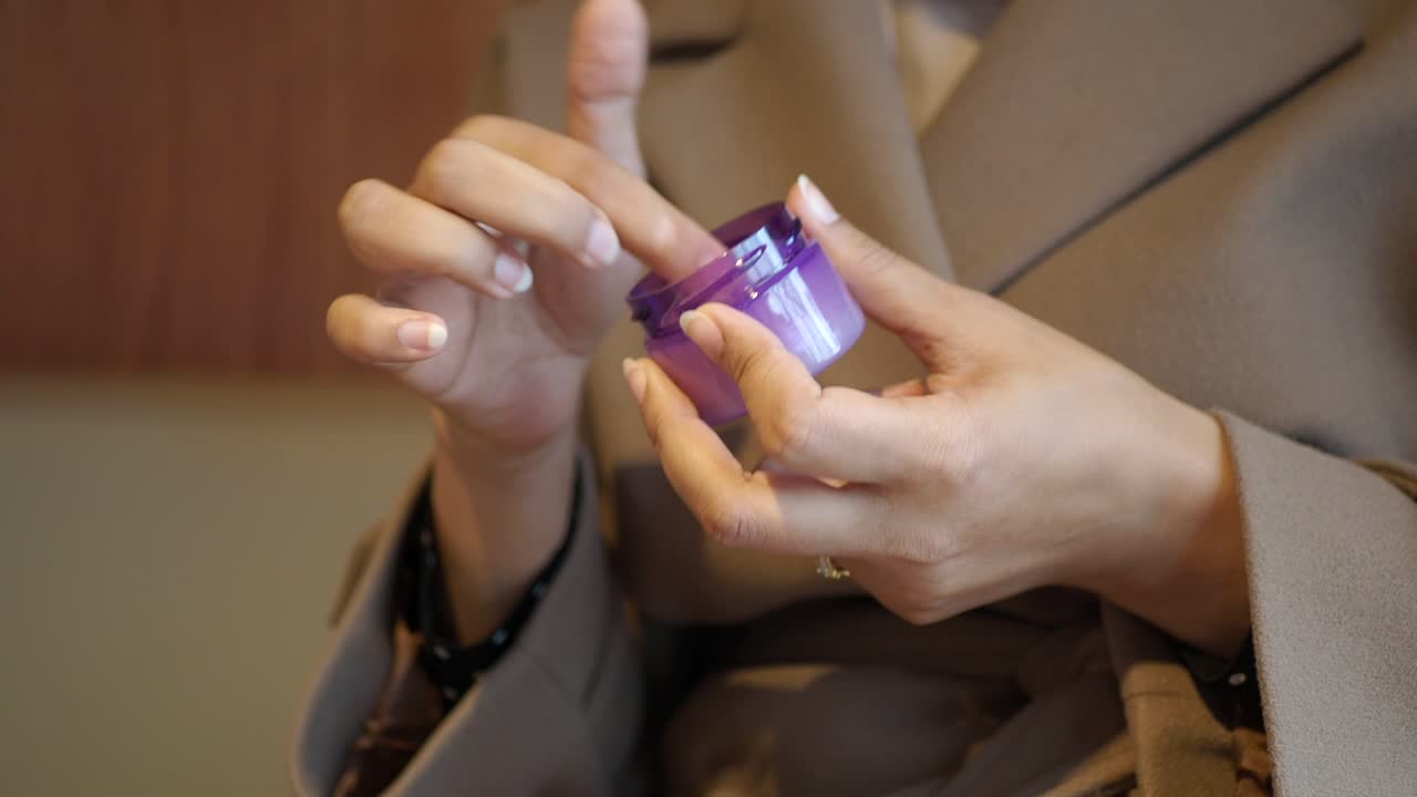 Nærbillede af hænder, der dypper finger i en krukke med lilla creme