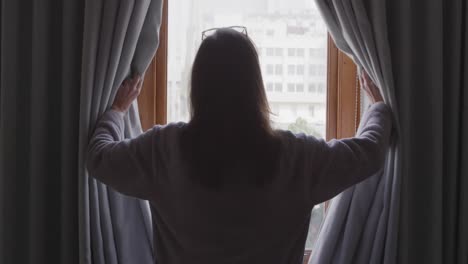 woman drawing curtains and looking out of the window at home