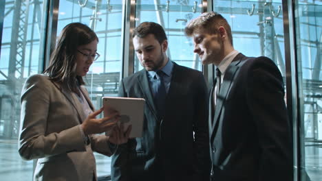 businesswoman and two businessmen in a elevator talking and looking a tablet