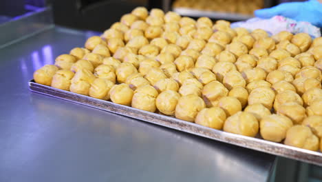 freshly baked profitroles being taken off the oven. factory worker pulls the baking sheet from oven and puts it on the table. close up.