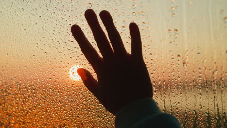 silueta oscura de la mano en la ventana con gotas en la lluvia de cerca la palma elegante expresa la angustia