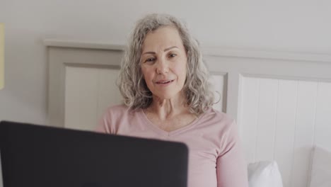 happy senior caucasian woman sitting on bed using laptop, slow motion