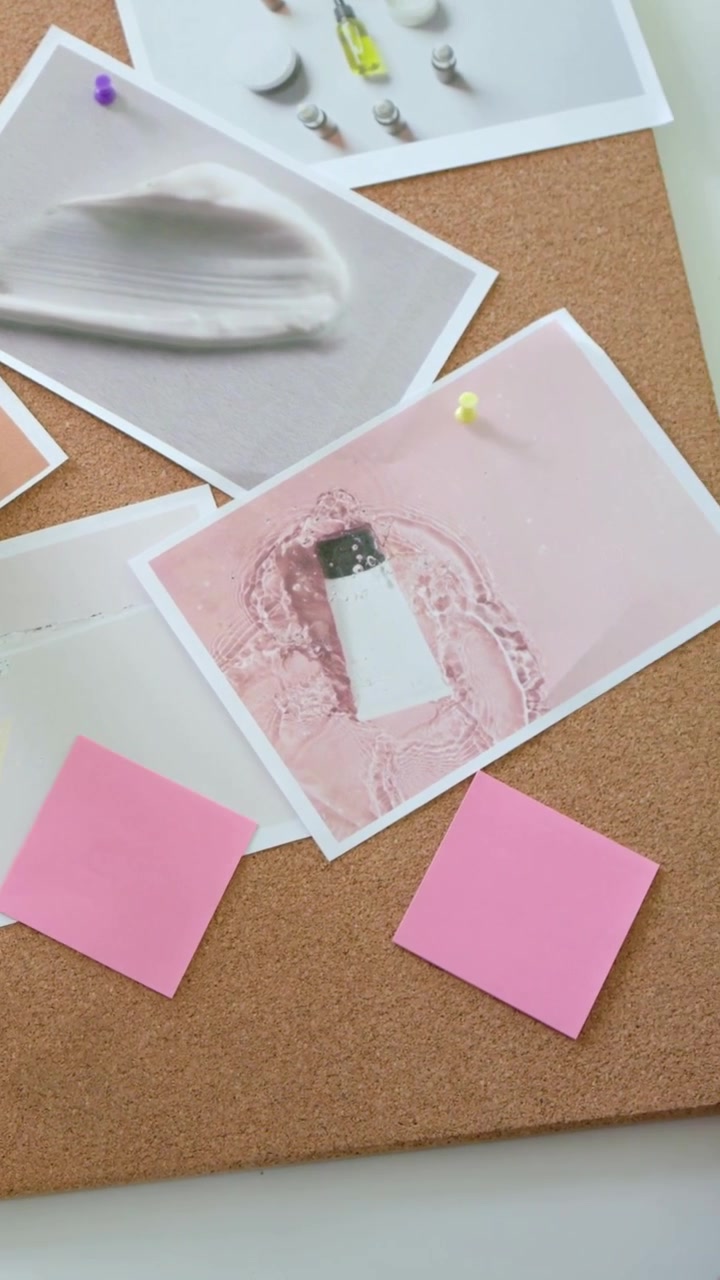 Video verticale: Donna che si china e appunta una stampa su una bacheca di sughero alla scrivania, creando una mood board con delle puntine.