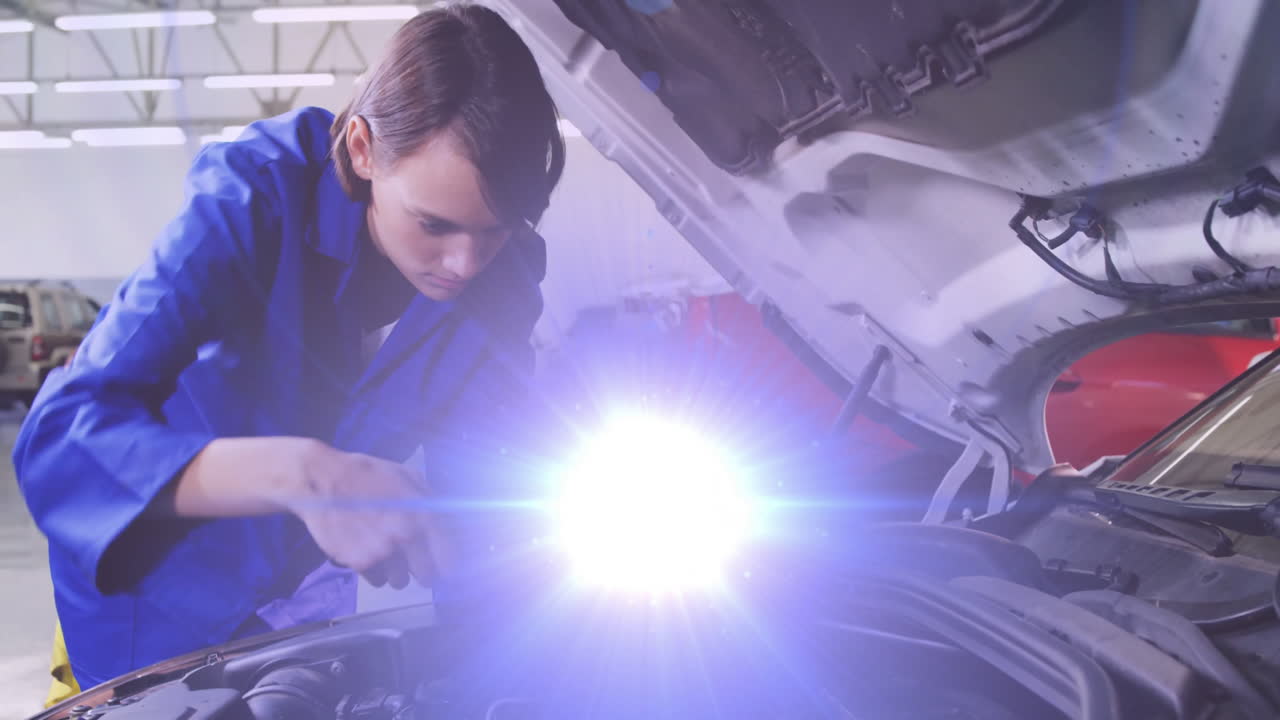 Female mechanic working under inspection light in auto garage, showing animated engine data