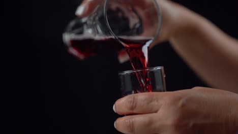 manos de mujer vertiendo bebida roja de un vaso en otro