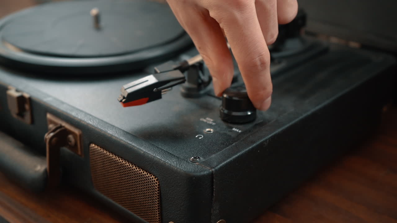 A hand turns down the volume of a turntable.