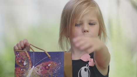 a happy young blonde-haired girl with a gift bag in her hands