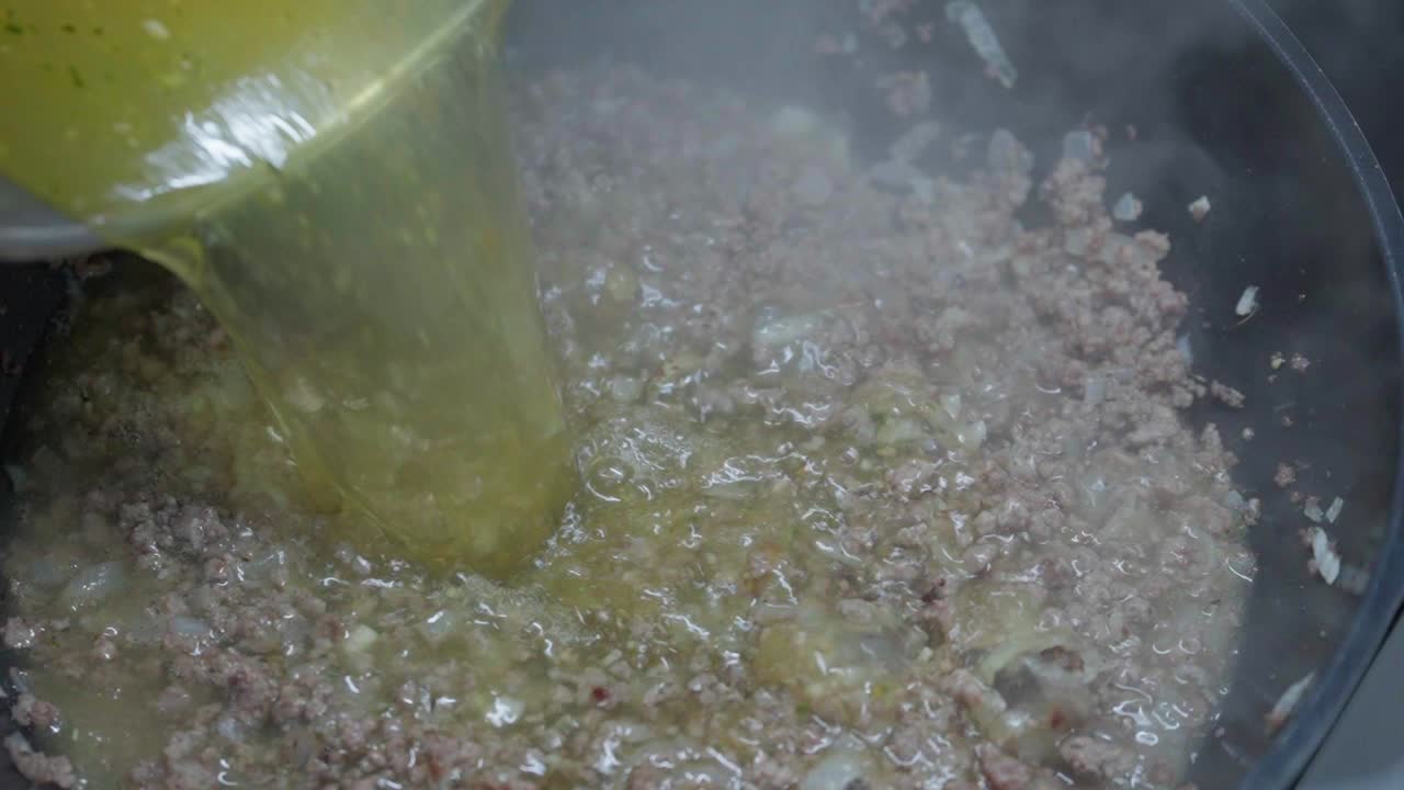 Broth poured over minced meat and onion in pan during home food cooking process