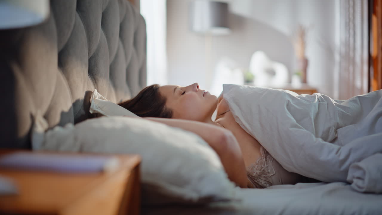 Sleepy lady waking up in sunlit hotel room closeup. Brunette sitting on pillows