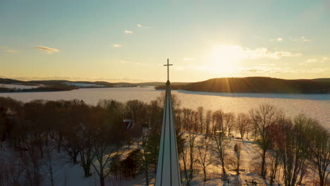 Vista-Aérea-Escénica-De-Un-Campanario-De-La-Iglesia-Contra-Una-Puesta-De-Sol-De-Invierno-A-Través-De-Un-Lago-Congelado