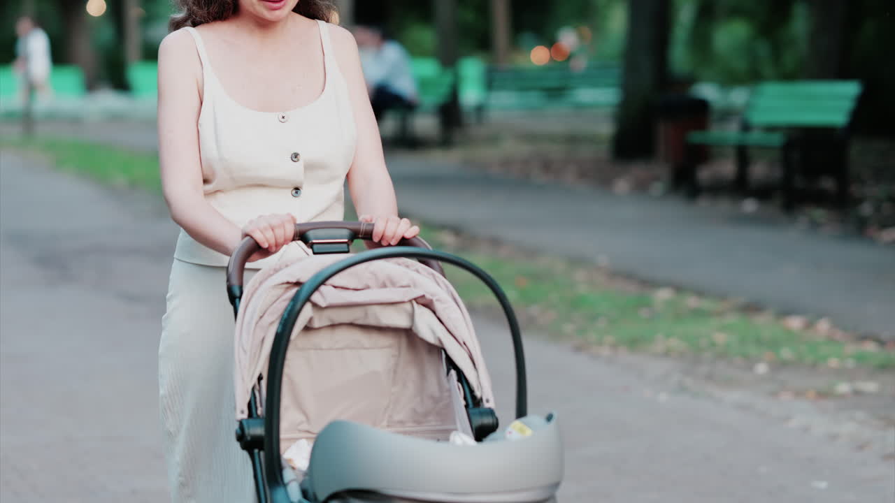 Mother dressed in light summer clothes pushing a baby stroller along a quiet park street