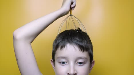 a caucasian boy enjoy head scalp massage by anti stress acupuncture metal octopus tool, equipment, she closes her eyes with pleasure, yellow background, close up view