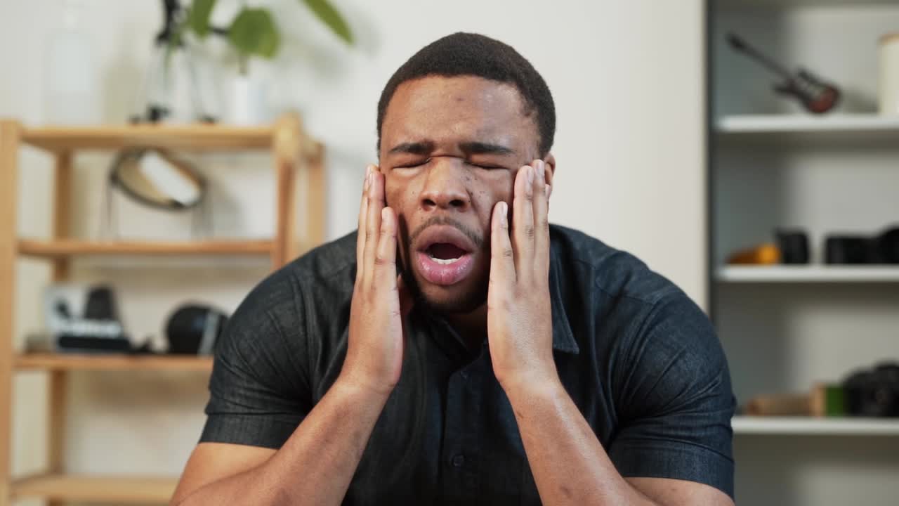 A dark-skinned man holds his head trying to overcome a migraine