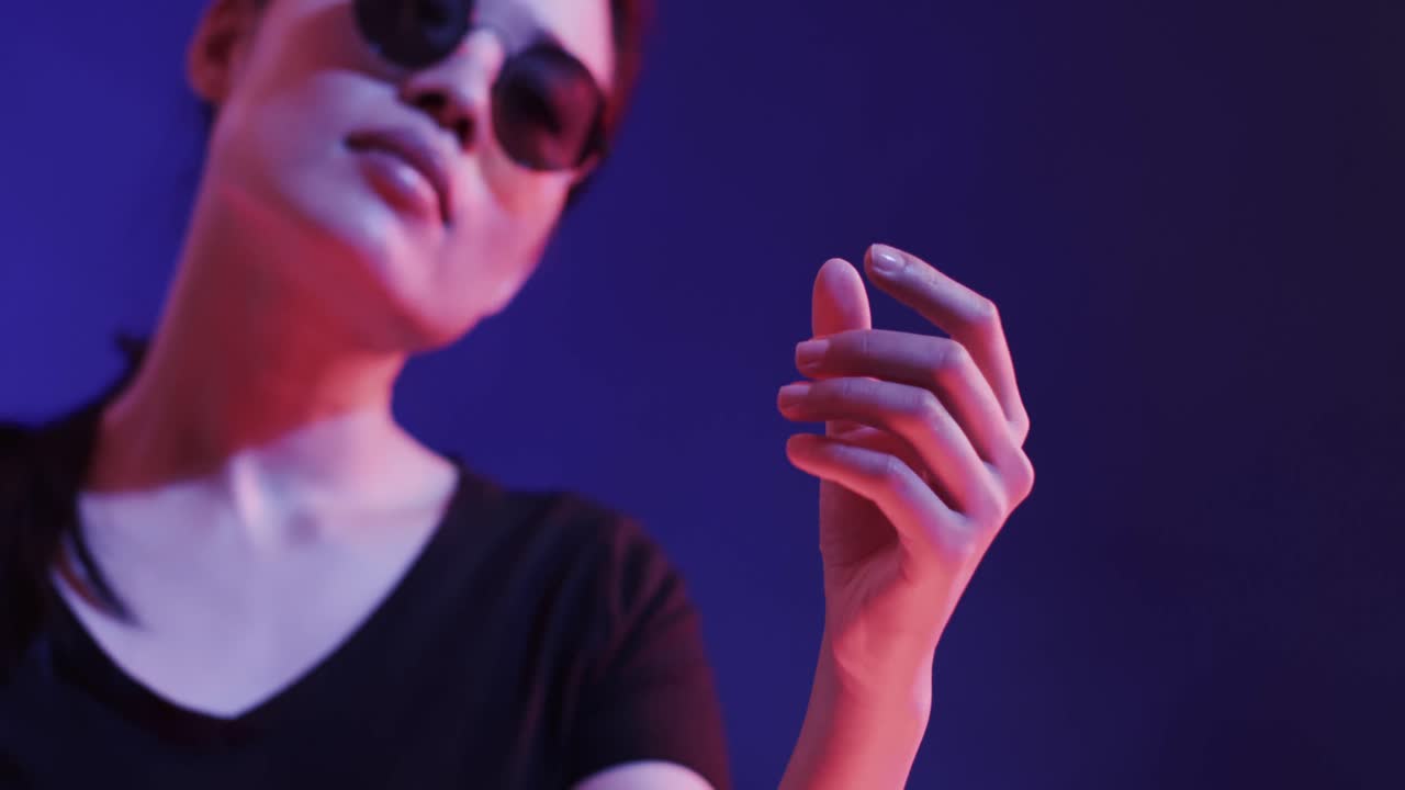 Asian woman wearing black glasses, touching virtual screen on blue background, slow motion