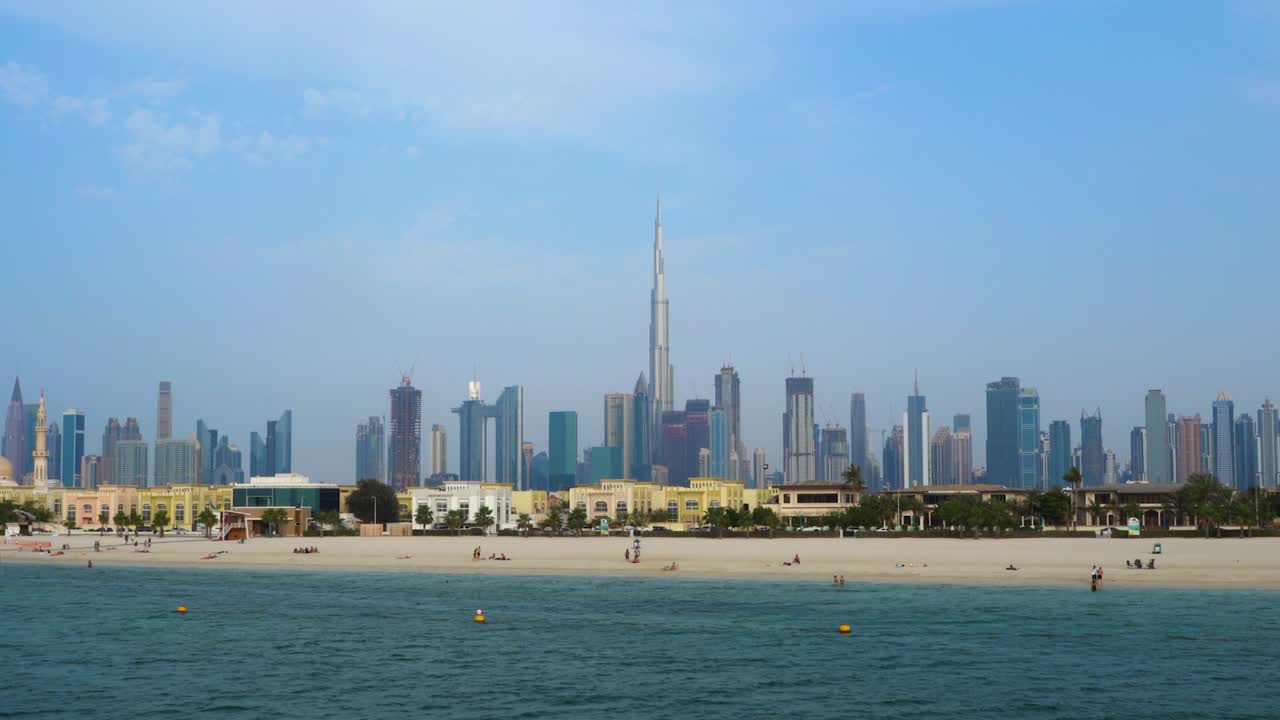 Turisti sulla riva della spiaggia di Jumeirah con il centro di Dubai e il Burj Khalifa negli Emirati Arabi Uniti