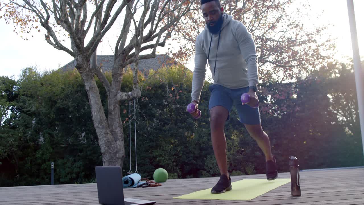 hombre afroamericano entrenamiento de fitness haciendo ejercicios con pesas en cubierta en jardín soleado, cámara lenta