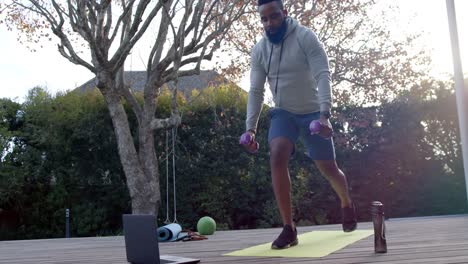 african american man fitness training exercising with weights on deck in sunny garden, slow motion