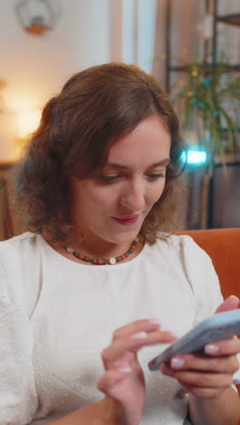 happy smiling woman sitting on couch using smartphone texting smiling at home living room apartment
