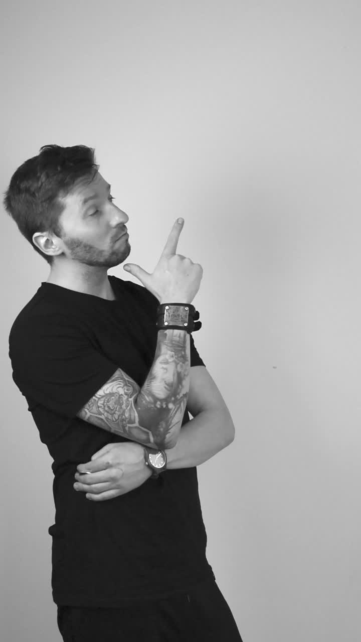 Grayscale footage of a white tattooed male with short hair and beard looking into a empty corner on a white background on the upper right side and thinks about it while putting hand on chip, points it