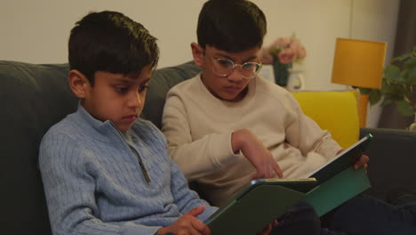 two young boys sitting on sofa at home playing games or streaming onto digital tablets 6