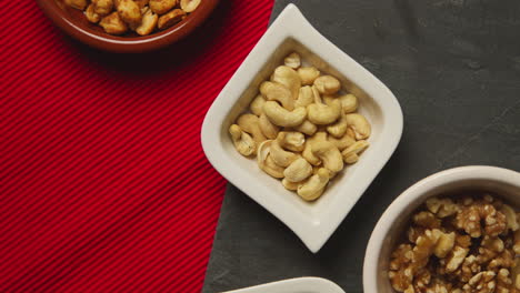 close up overhead shot of bowls containing cashews dry roasted peanuts pistachio walnuts and hazelnut nuts revolving