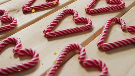 animation of golden star icons over close up of candy cane on wooden surface