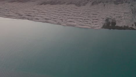 Drone-shot-flying-above-the-sea-near-sand-dunes-landscape-at-day,-wide-angle