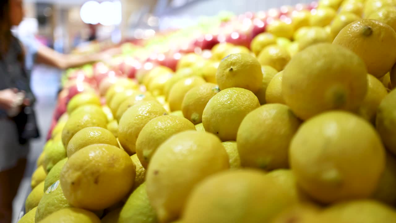 A woman selects lemons in a brightly lit Gold Coast supermarket. Vibrant colors and dynamic camera angles capture the bustling environment