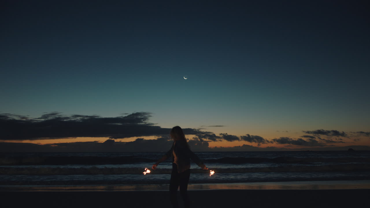 일몰 때 해변에서 축하하는 빛나는 여자 바다에서 새해 전야 축하를 즐기고 즐거운 춤을 추는 소녀