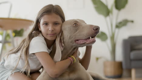 retrato de una niña abrazando y acariciando a su adorable perro en casa y mirando la cámara