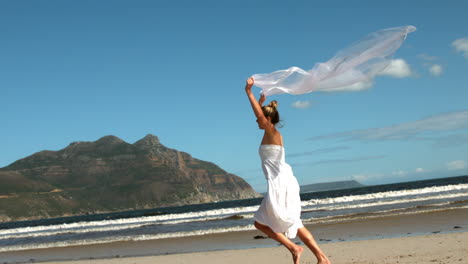 carefree blonde running on the beach holding scarf up