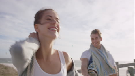 young couple holding hands woman leading boyfriends walking towards sunset on empty beach