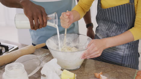 Mid-section-of-diverse-couple-wearing-apron-and-baking-in-kitchen